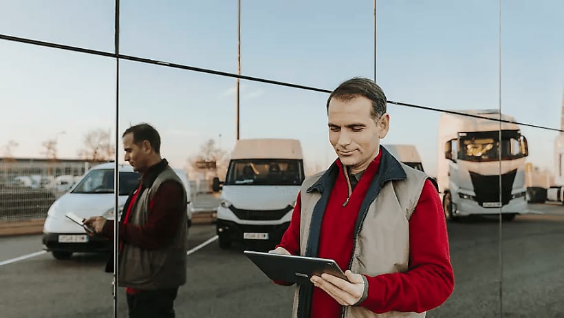 Wagenparkbeheerder die op een parkeerplaats staat en een tablet in handen heeft.